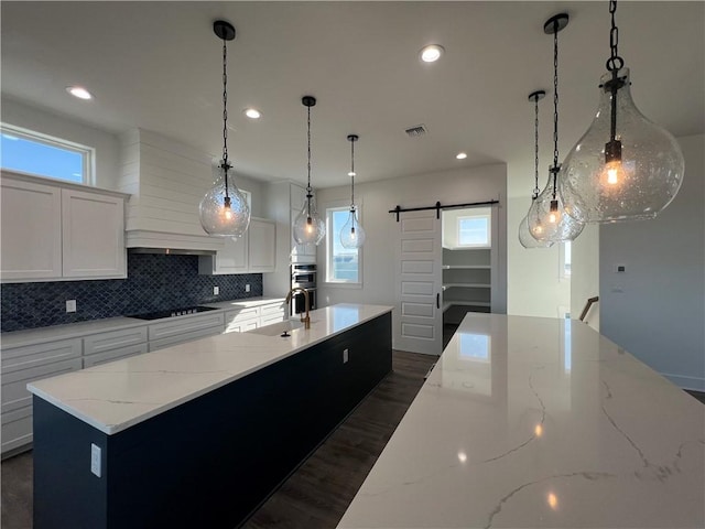 kitchen featuring visible vents, a spacious island, a barn door, black electric cooktop, and backsplash