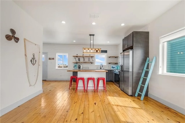 162 La Concha Blvd Unit 20, Port Aransas, TX 78373 - kitchen featuring open shelves, light wood-type flooring, a breakfast bar, stainless steel refrigerator with ice dispenser, and a kitchen island