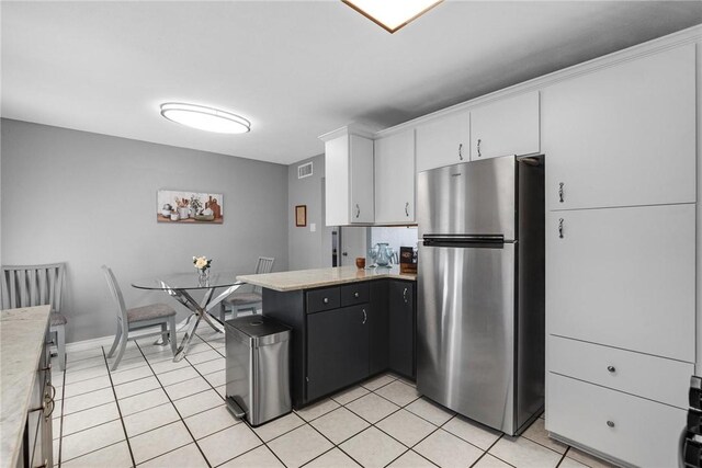 kitchen featuring stainless steel fridge, light tile patterned floors, and white cabinets