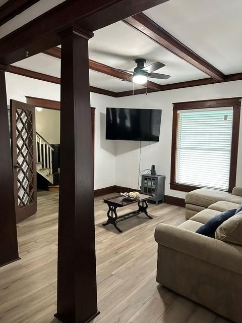 living room with stairs, baseboards, beam ceiling, and light wood-style floors