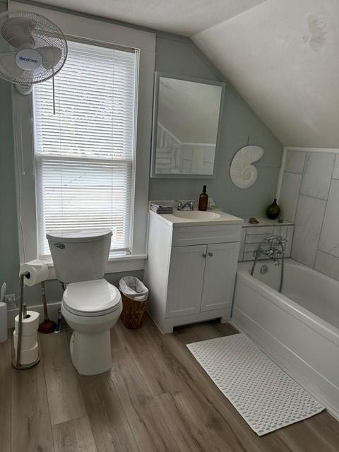 bathroom featuring lofted ceiling, toilet, wood finished floors, and a bath