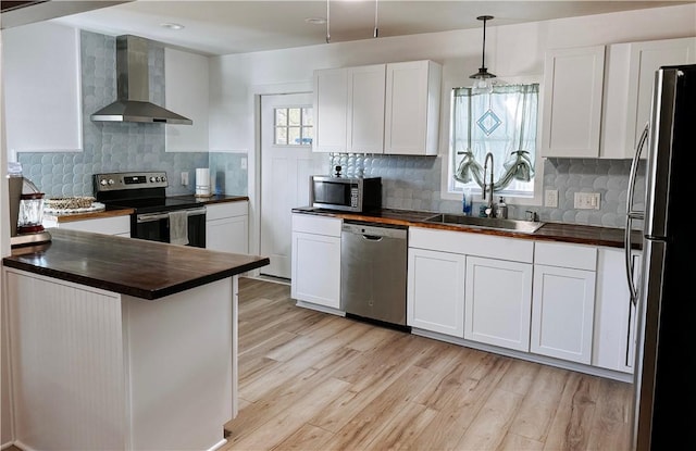 kitchen featuring a sink, white cabinets, appliances with stainless steel finishes, light wood-type flooring, and wall chimney exhaust hood