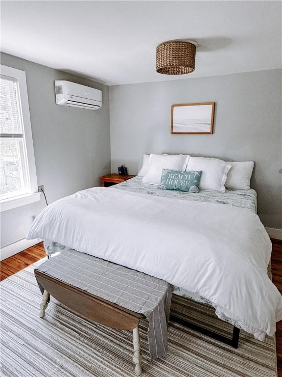 bedroom featuring a wall unit AC, baseboards, and wood finished floors