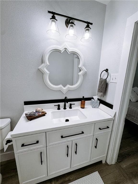 bathroom with a textured wall, vanity, toilet, and wood finished floors