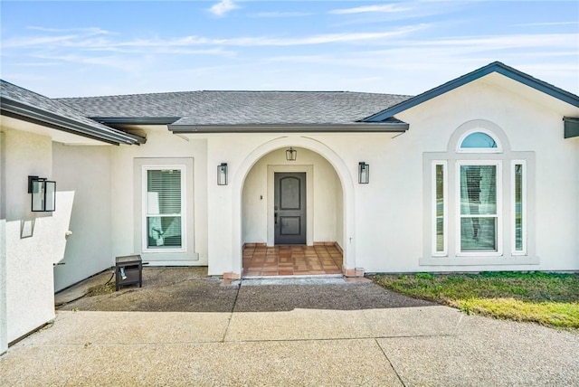 doorway to property featuring a shingled roof and stucco siding