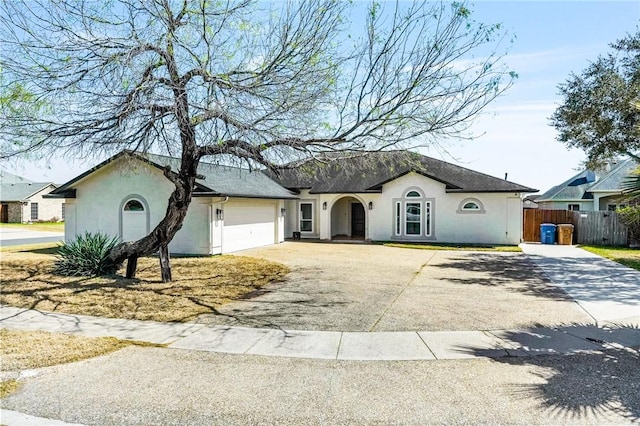 ranch-style home featuring driveway, an attached garage, fence, and stucco siding