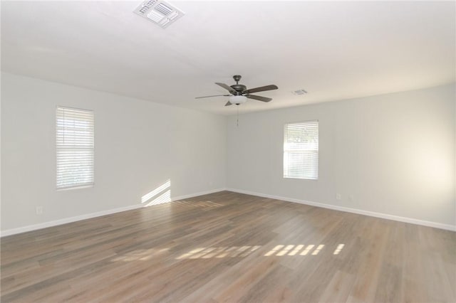 unfurnished room featuring a ceiling fan, wood finished floors, visible vents, and baseboards