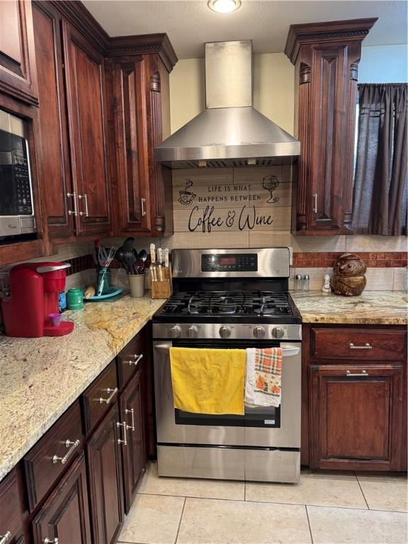 1101 N Adams St N, Beeville, TX 78102 - kitchen featuring wall chimney exhaust hood, stainless steel gas range oven, light tile patterned flooring, and light stone countertops