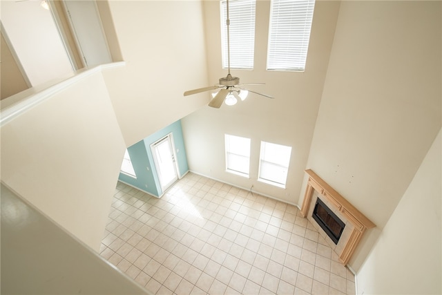 unfurnished living room with a towering ceiling, a fireplace, ceiling fan, and light tile patterned flooring