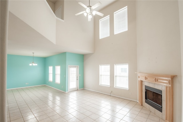 unfurnished living room with a fireplace, ceiling fan with notable chandelier, light tile patterned floors, and a high ceiling