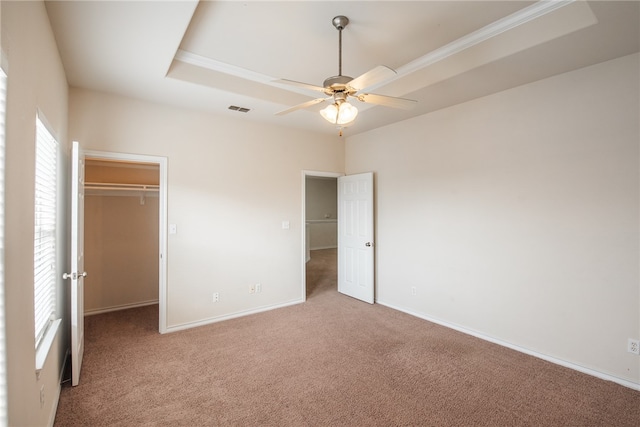 unfurnished bedroom with light carpet, ceiling fan, a spacious closet, a tray ceiling, and a closet