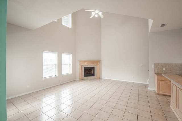 unfurnished living room featuring a towering ceiling, ceiling fan, light tile patterned floors, and a tiled fireplace