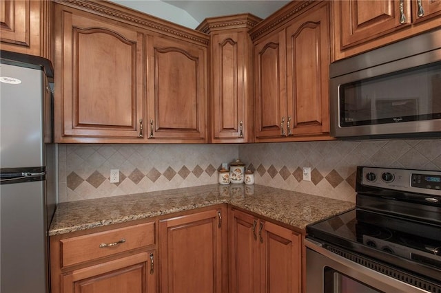 kitchen featuring light stone counters, backsplash, stainless steel appliances, and brown cabinets