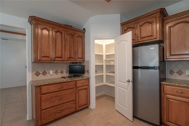 kitchen with light tile patterned floors, light stone countertops, brown cabinets, and freestanding refrigerator