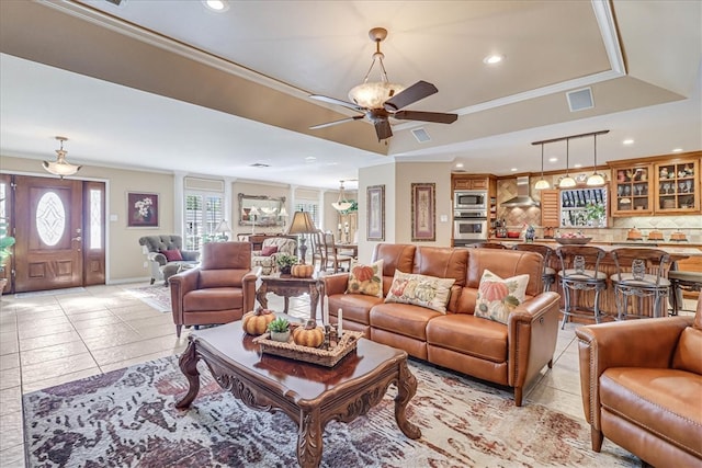 tiled living room featuring ceiling fan, a tray ceiling, and ornamental molding