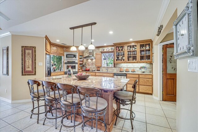 kitchen with crown molding, stainless steel appliances, backsplash, light stone countertops, and a center island