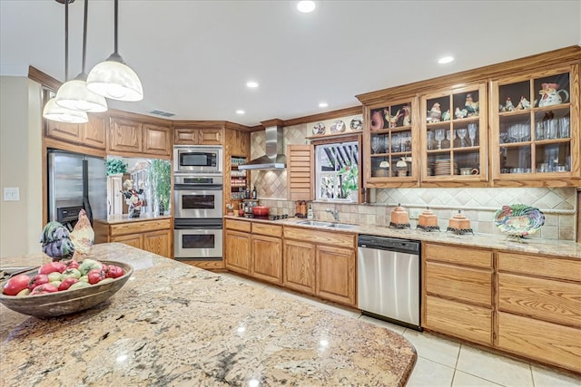 kitchen featuring light stone counters, appliances with stainless steel finishes, hanging light fixtures, sink, and wall chimney exhaust hood