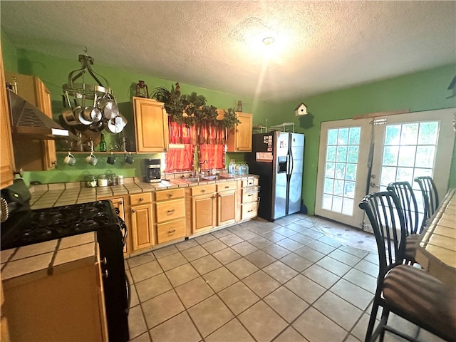 kitchen with extractor fan, a textured ceiling, stainless steel refrigerator with ice dispenser, tile counters, and electric range