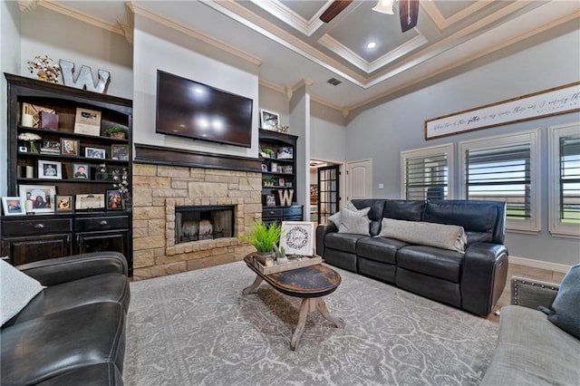 living room with a stone fireplace, ceiling fan, coffered ceiling, and ornamental molding