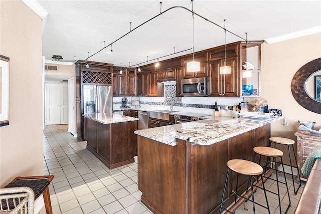 kitchen featuring light stone counters, a peninsula, a sink, decorative backsplash, and appliances with stainless steel finishes