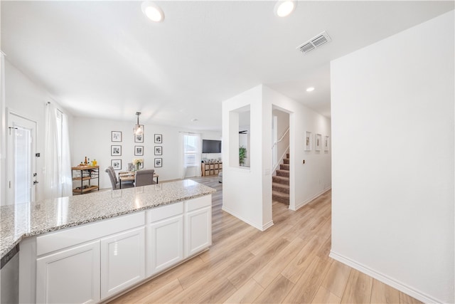 kitchen with white cabinetry, pendant lighting, light stone counters, and light hardwood / wood-style floors