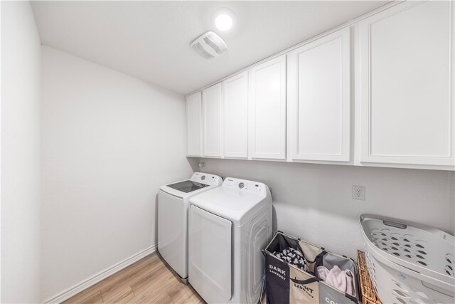 clothes washing area with cabinets, washing machine and dryer, and light hardwood / wood-style flooring