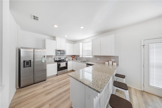 kitchen featuring stainless steel appliances, white cabinetry, sink, a kitchen breakfast bar, and light wood-type flooring