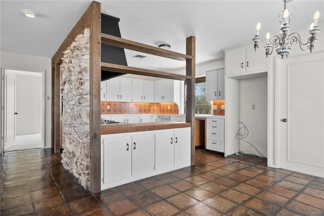 kitchen with a chandelier, white cabinets, decorative light fixtures, stone tile flooring, and stainless steel gas cooktop