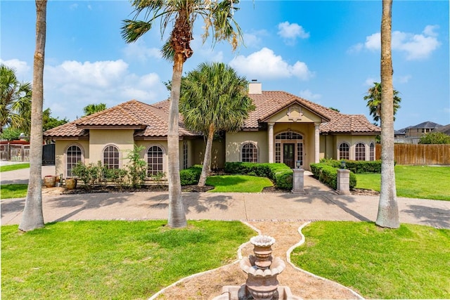 mediterranean / spanish house with a tile roof, a chimney, fence, a front lawn, and stucco siding