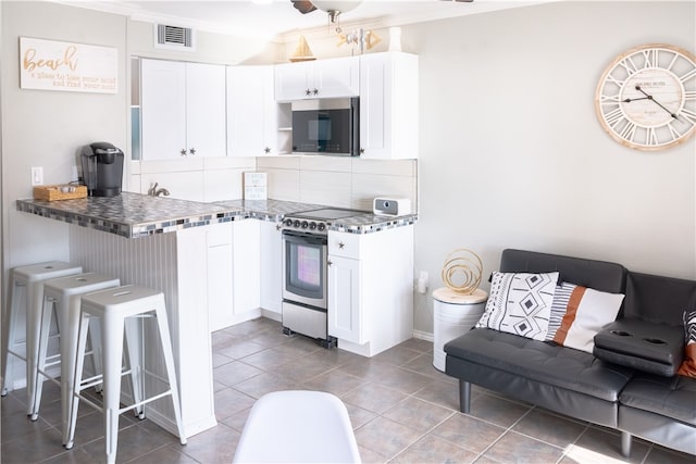 kitchen featuring tasteful backsplash, white cabinets, a kitchen bar, and stainless steel appliances