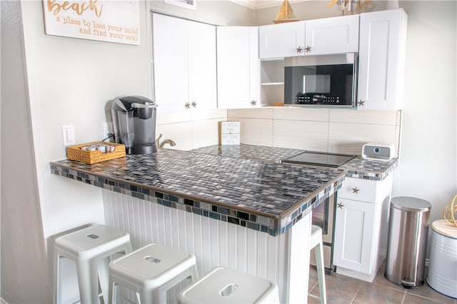 kitchen with a kitchen breakfast bar, white cabinetry, light tile patterned floors, and black electric stovetop