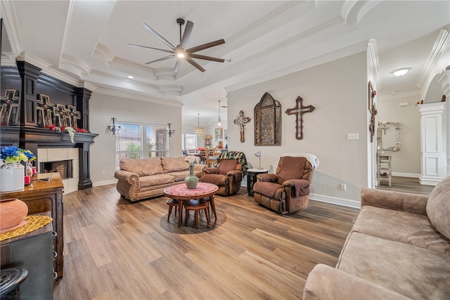 living room with a tiled fireplace, wood-type flooring, ceiling fan, crown molding, and a tray ceiling