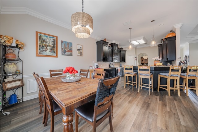 dining area with a chandelier, light wood-type flooring, vaulted ceiling, and ornamental molding