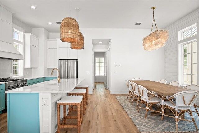 kitchen featuring stainless steel fridge, light hardwood / wood-style floors, decorative light fixtures, a center island with sink, and white cabinets