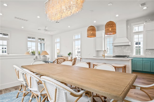 dining room with a healthy amount of sunlight, ceiling fan with notable chandelier, and light hardwood / wood-style floors