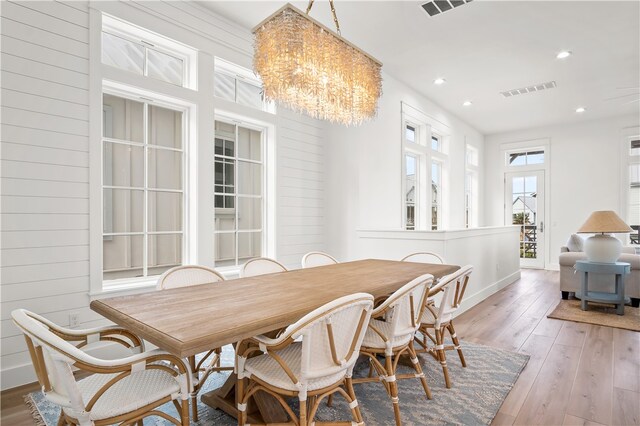 dining room featuring an inviting chandelier, wooden walls, and light hardwood / wood-style flooring