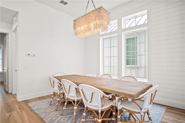 dining room with wood walls, light hardwood / wood-style flooring, and a chandelier