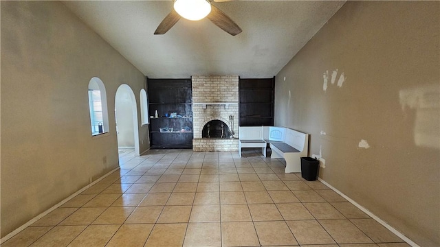 unfurnished living room with light tile patterned floors, a brick fireplace, and ceiling fan