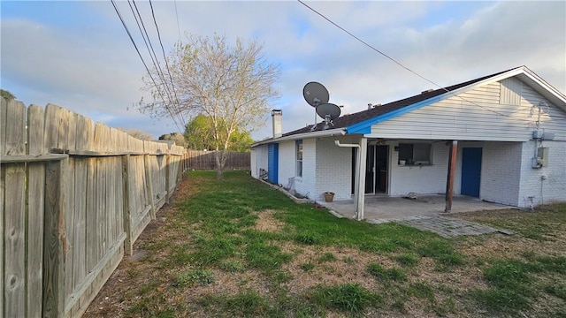 rear view of house featuring a fenced backyard, brick siding, a lawn, a chimney, and a patio area