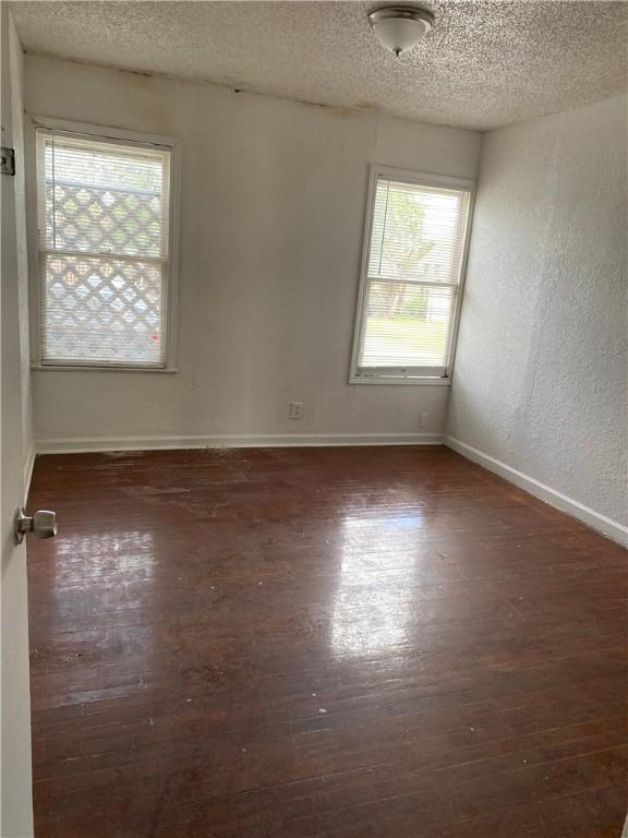 empty room with a textured ceiling, a textured wall, wood finished floors, and baseboards