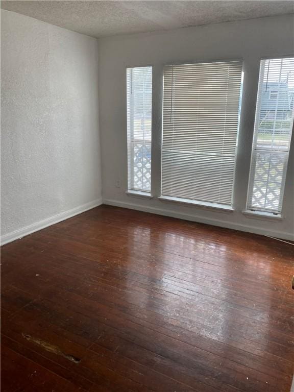 spare room featuring a textured ceiling, a textured wall, wood-type flooring, and baseboards