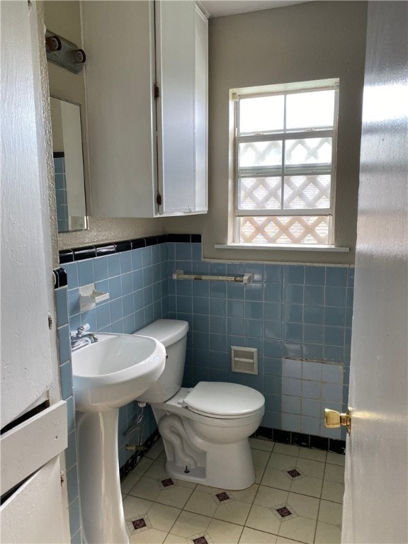 bathroom with a wainscoted wall, tile walls, toilet, and tile patterned floors