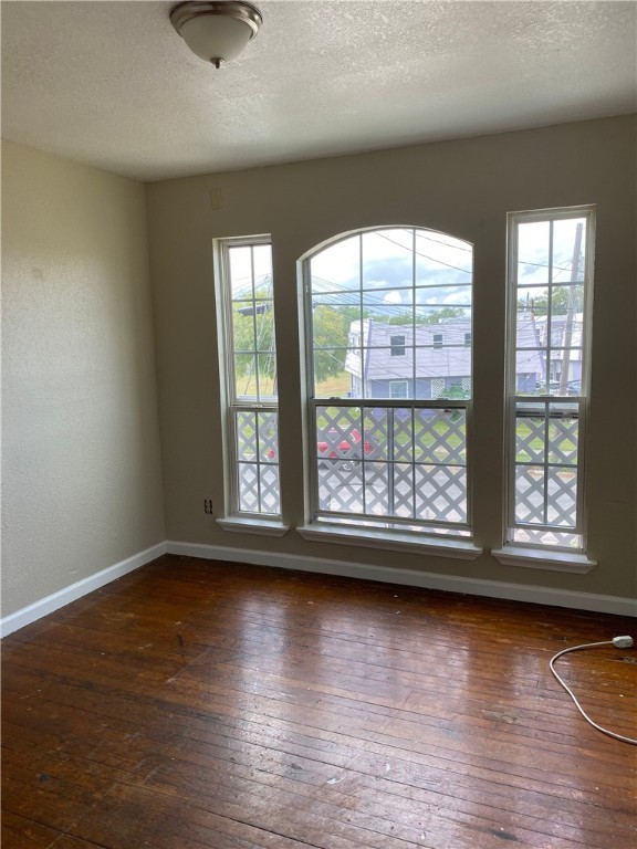 spare room with baseboards, a textured ceiling, and hardwood / wood-style floors