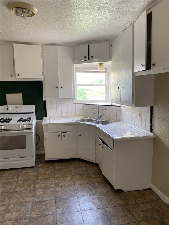 kitchen with tile counters, white cabinets, backsplash, and white gas range