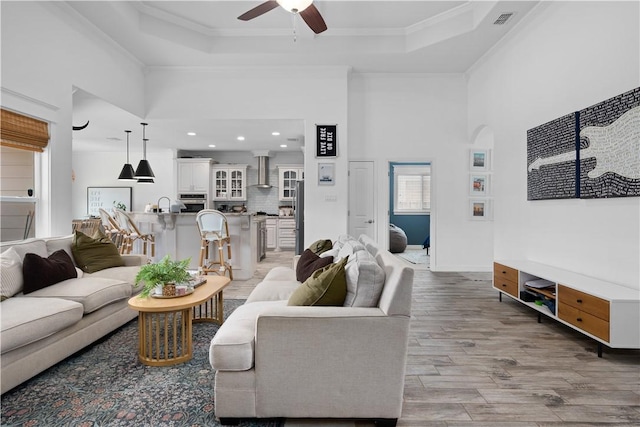 15114 Barataria Dr, Corpus Christi, TX 78418 - living room featuring ceiling fan, a tray ceiling, light wood-style flooring, ornamental molding, and a high ceiling