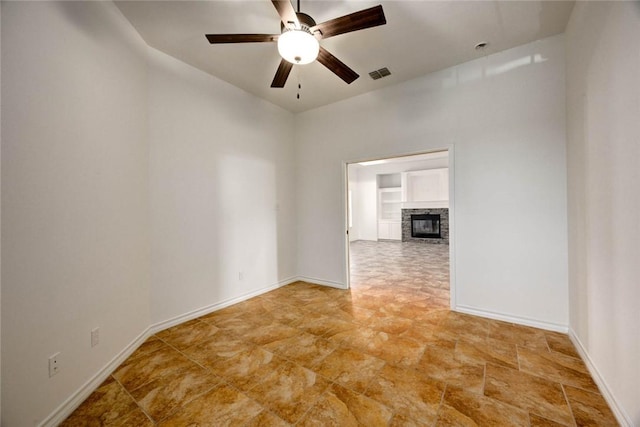 spare room with a stone fireplace and ceiling fan