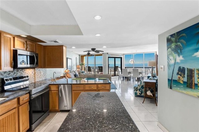 kitchen with hanging light fixtures, dark stone countertops, light tile patterned floors, appliances with stainless steel finishes, and backsplash