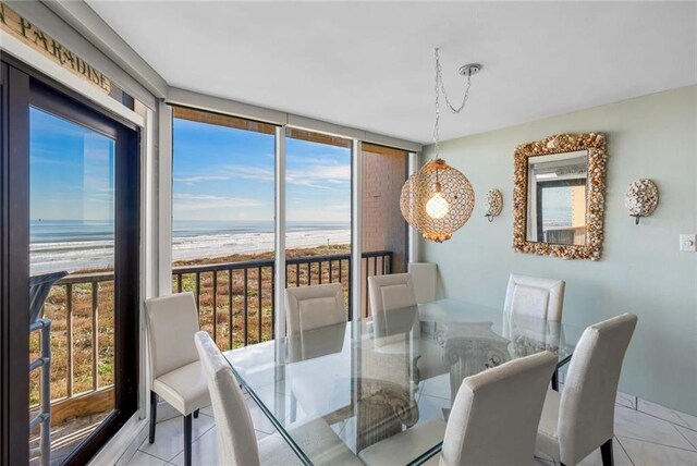 dining room featuring a view of the beach, a water view, floor to ceiling windows, and light tile patterned floors