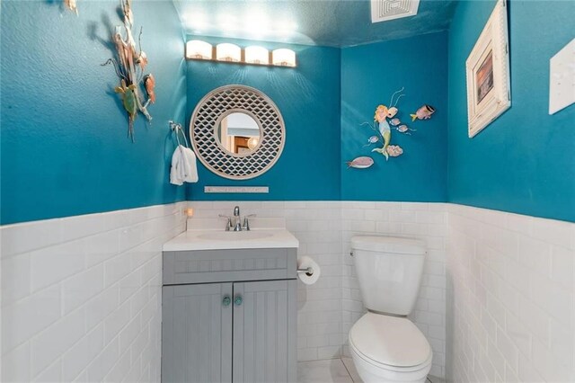 bathroom featuring vanity, tile walls, and toilet