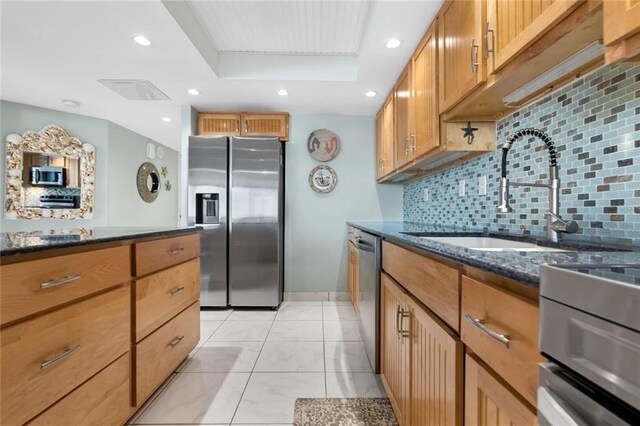 kitchen featuring sink, appliances with stainless steel finishes, dark stone countertops, tasteful backsplash, and a raised ceiling